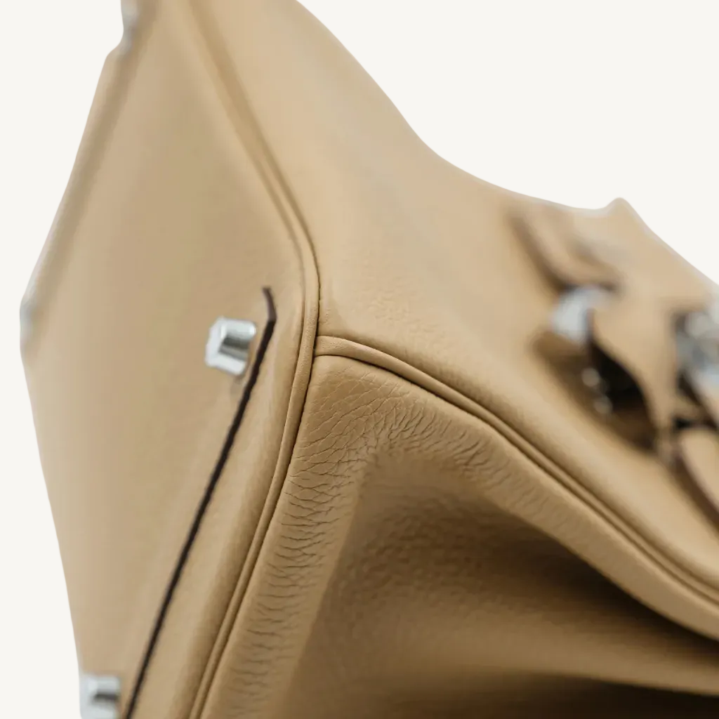 Close-up of a beige leather handbag with silver hardware on a white background
